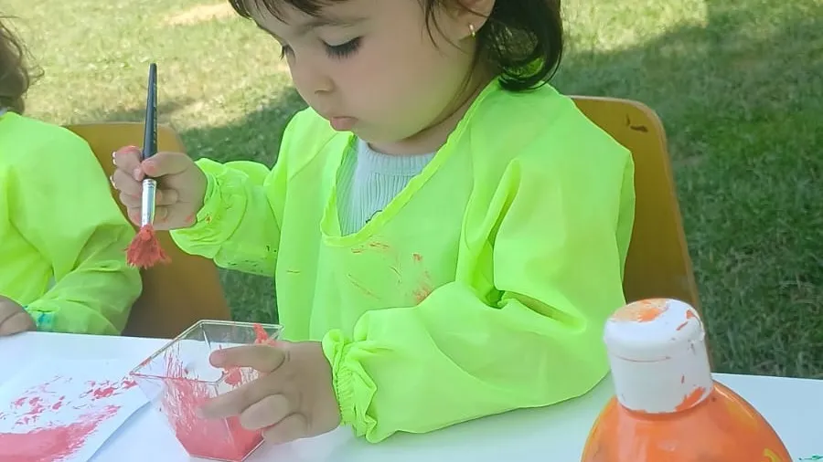 Önlüğünü giymiş bir çocuk atölye masasında fırçayla boya çalışması yapıyor