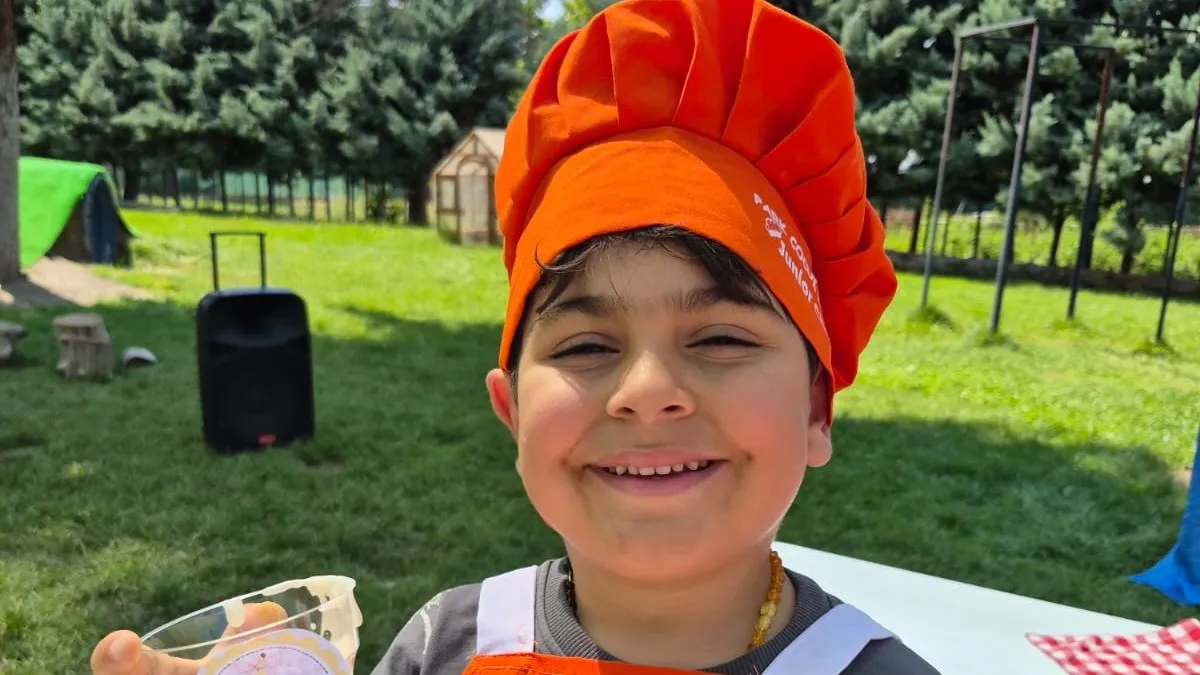 Turuncu aşçı şapkası ve önlüğüyle gülümseyen bir çocuk, Junior Chef etkinliği
